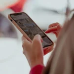 Hands holding a smartphone, browsing social media outdoors on a sunny day.
