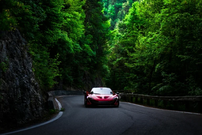 A sleek red supercar driving through a lush green forest road, capturing speed and elegance.
