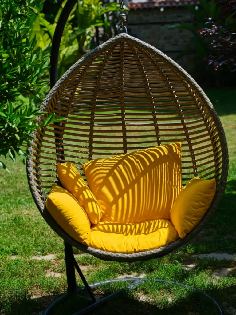 Relax in a stylish hanging egg chair with bright yellow cushions, set in a tranquil garden.