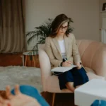 Female therapist writing notes during a counseling session, focusing on mental health.