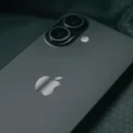 A stylish workspace featuring a laptop, smartphone, and tissue box on a glass table with a red patterned rug.