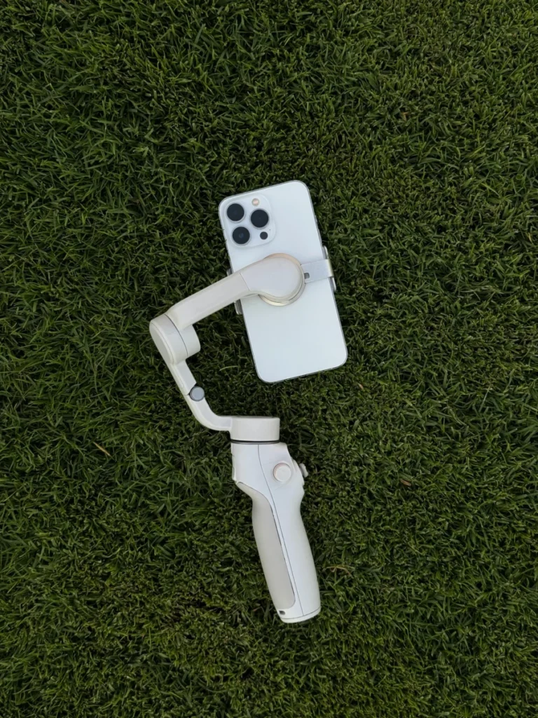 White smartphone attached to a gimbal lying on lush green grass outdoors in Dubai. Perfect for tech themes.