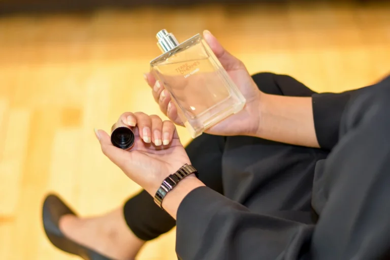 L’iPhone « Hermès orange » relance le succès d’Apple en Chine Close-up of a woman holding a Terre d'Hermes perfume bottle indoors, showcasing elegance and luxury.