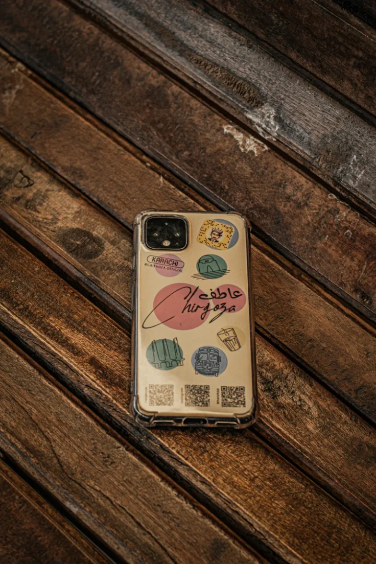 Close-up of a smartphone on a textured wooden table, featuring an artistic case with colorful designs.