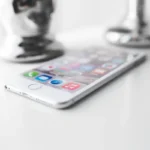 Close-up of a modern silver smartphone on a white surface with apps visible.