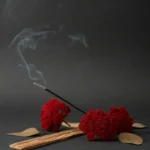 A calming still life featuring red dried flowers, incense with smoke, and wooden elements.