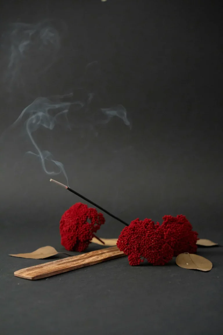 A calming still life featuring red dried flowers, incense with smoke, and wooden elements.