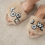 Furry slippers with 'Lockdown' text and feet on a soft carpet - a cozy home vibe.