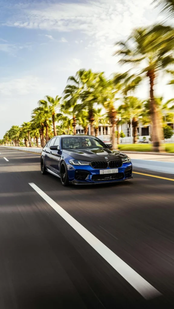 Dynamic shot of a blue car speeding down a palm-lined street in Kuwait City, exuding elegance and performance.