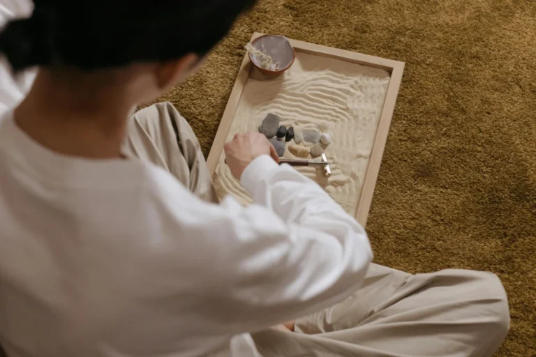 Over the shoulder view of a person arranging rocks in a mini zen garden on a rug.