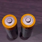 Top view of two AA batteries with yellow tops on a dark surface.