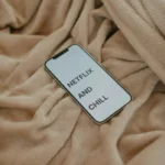 Smartphone displaying 'Netflix and Chill' on a beige blanket, ideal for cozy lifestyle themes.