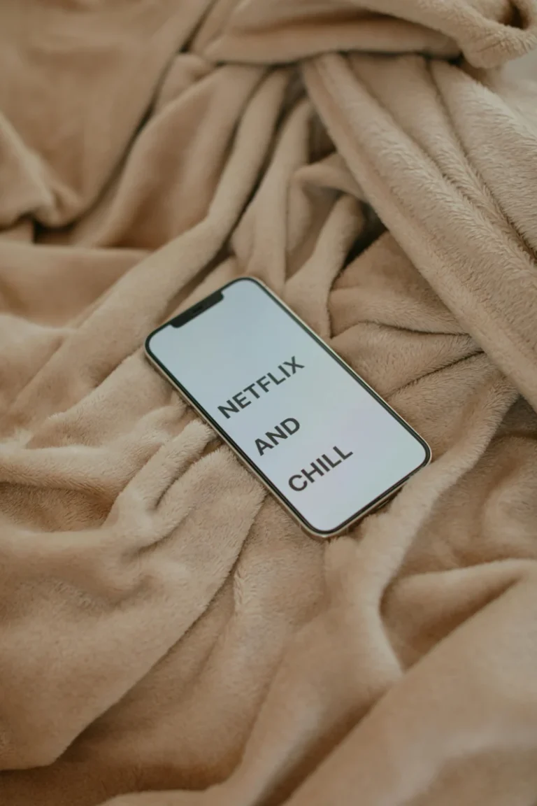 Smartphone displaying 'Netflix and Chill' on a beige blanket, ideal for cozy lifestyle themes.