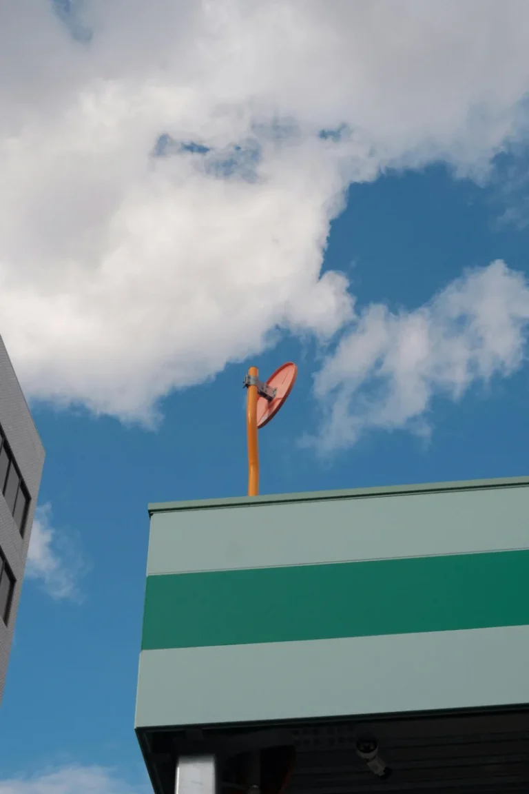 Modern building with orange satellite dish against a blue sky with clouds.