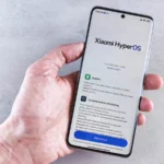 Close-up of a hand holding a Xiaomi smartphone with HyperOS interface, showcasing comprehensive refactoring and system update details.