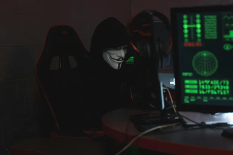 Apple corrige une faille zero-day exploitée impactant iOS, macOS et tous les appareils Apple An anonymous hacker wearing a Guy Fawkes mask sits at a computer in a dimly lit room, engaged in cyber activities.