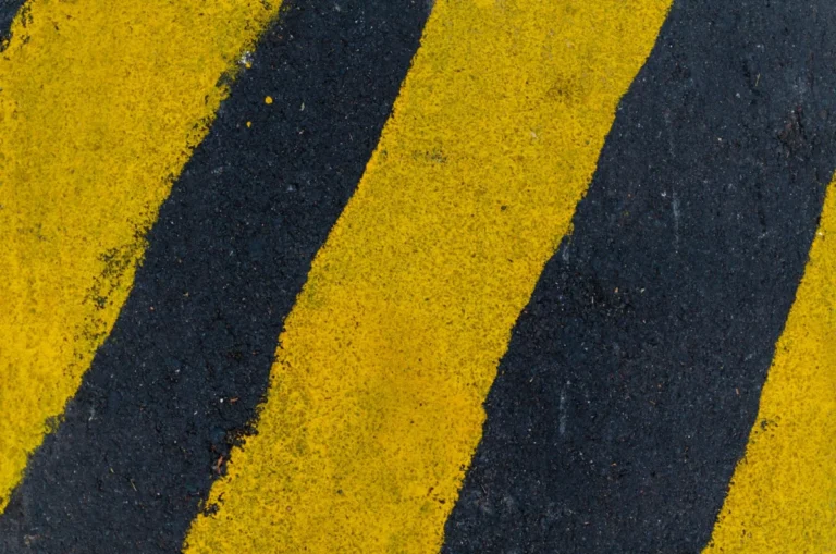 A high-angle close-up of yellow and black road markings on asphalt surface.