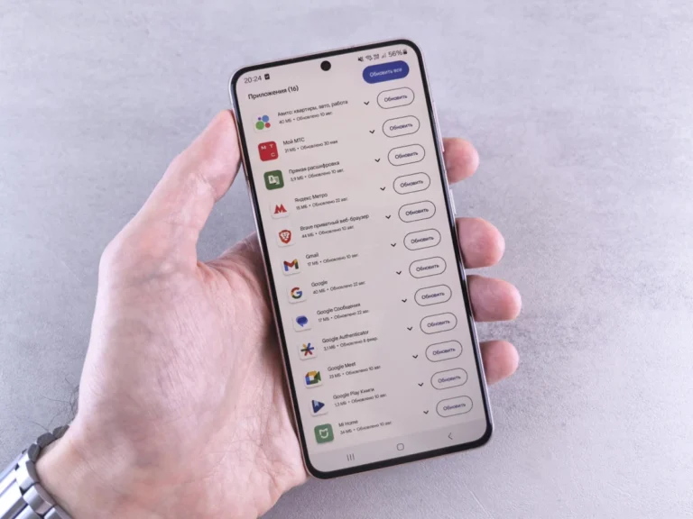Close-up of a hand holding a smartphone displaying app updates on a light background.