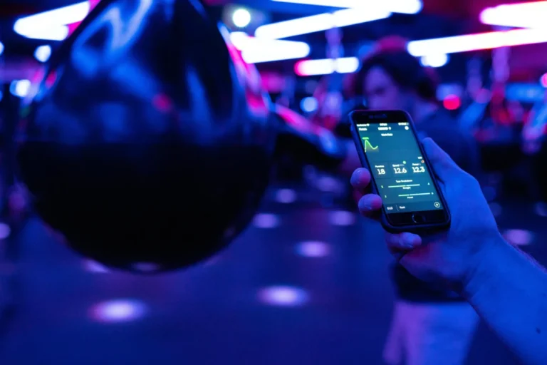 Smartphone displaying fitness tracking data next to boxing equipment under neon lighting.