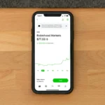 Stock trading app on smartphone displaying Robinhood Markets price on wooden desk.