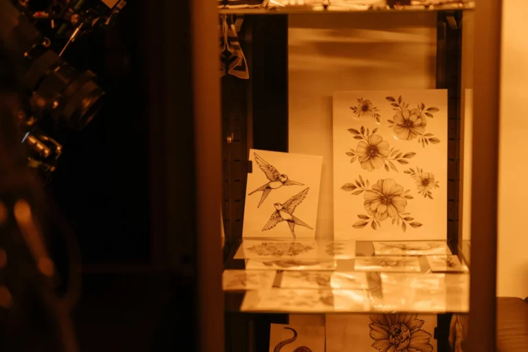 Tattoo sketches of birds and flowers displayed in a tattoo studio under warm lighting.