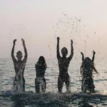 Silhouettes of four people joyfully splashing water in the sea during a beautiful sunset.