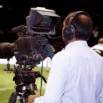 A cameraman filming a soccer match in a stadium, capturing the action on video.