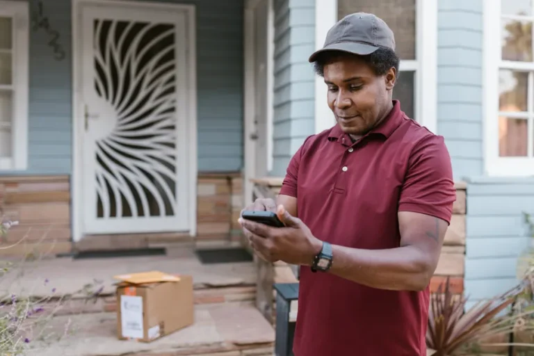 Vol de données DoorDash confirmé le 20 novembre 2025 : combien de clients? A courier in a maroon shirt checks delivery details on his phone at a residential porch with parcels.