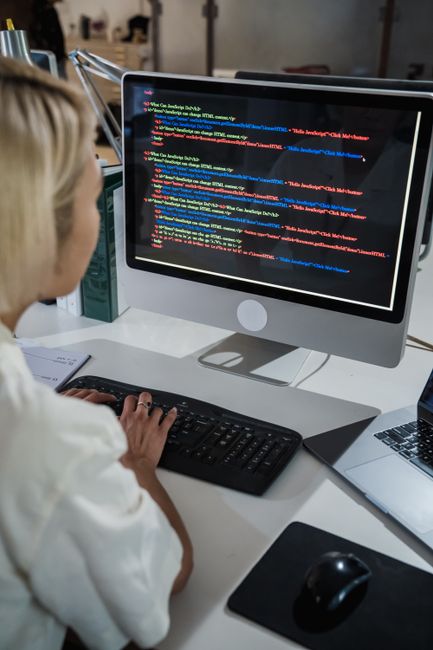 A female programmer writing code on a desktop computer in an office setting with a focus on technology and IT development.