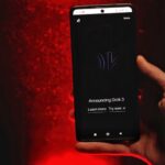Grok passe de la 6e à la 12e place dans l’App Store : xAI attaque Apple et OpenAI A hand holds a smartphone displaying Grok 3 announcement against a red background.
