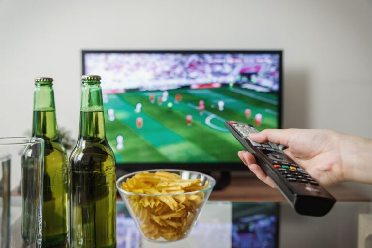 MLS Season Pass disparaît en 2026 : Apple TV change de match A person holding a remote while watching soccer on TV with beer and snacks on the table.