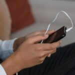 A person holds a smartphone with earbuds connected, capturing modern technology engagement.