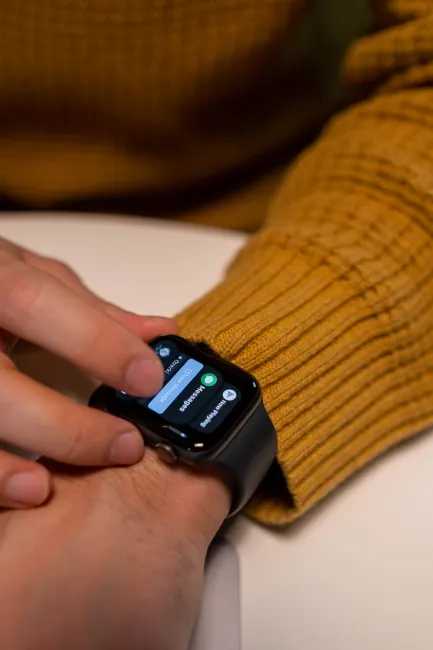 A person wearing a yellow sweater interacts with a smartwatch, focusing on the touch interface.