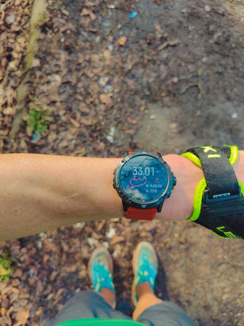 A runner checks a smartwatch displaying distance, time, and calories after an outdoor trail run.