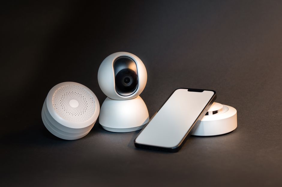 A sleek smartphone with modern smart home devices on a minimalist gray background.