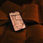 Pluribus : Apple Books offre un chapitre de Bloodsong of Wycaro le 14 novembre 2025 A smartphone displaying pages lies among open books, symbolizing digital integration.