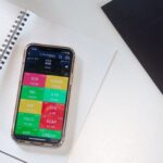 iPhone 16e « raté »? L’iPhone 17e attendu au printemps 2026 A smartphone displays a financial stock market app on a desk with a notebook and pencil.