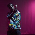 A vibrant rapper energetically performing on an indoor stage under bright lights.