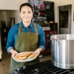 Awkwafina prépare une série Apple TV en 8 épisodes, sans recette miracle A woman in a kitchen holding a plate of food next to a large pot, showcasing homemade cooking.