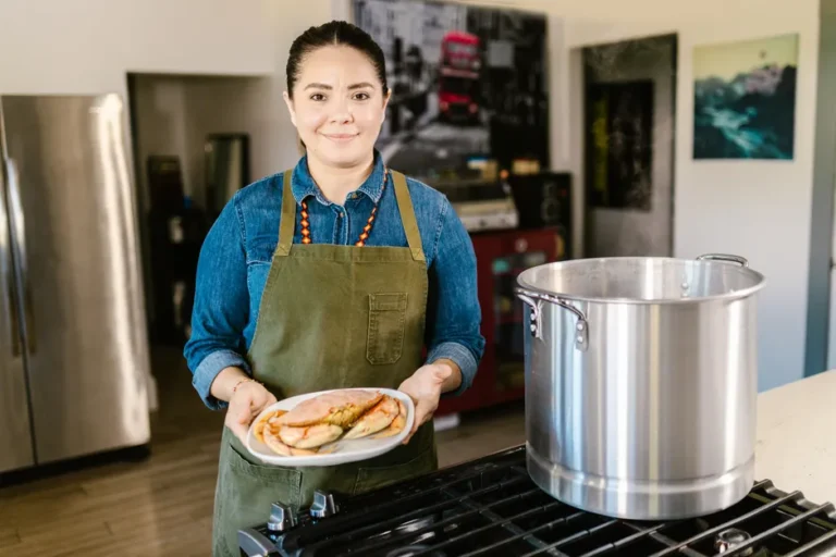 Awkwafina prépare une série Apple TV en 8 épisodes, sans recette miracle A woman in a kitchen holding a plate of food next to a large pot, showcasing homemade cooking.