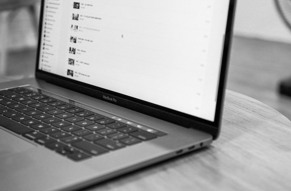 Black and white photo of a MacBook Pro on a round wooden table.