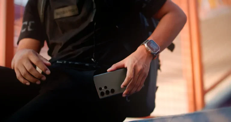 Apple Watch Ultra 2 à 599 dollars chez Amazon: le Black Friday 2025 taille dans le prix Casually dressed man with smartphone and smartwatch sitting outdoors, focusing on technology.