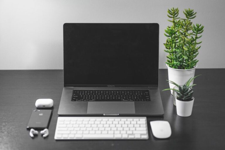 Clean and organized desk setup featuring a laptop, smartphone, and plants for a modern workspace vibe.