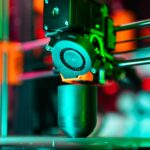 Le prototype OpenAI sort du brouillard, Jony Ive vise 2027 Close-up of a 3D printer creating a product in neon lighting.