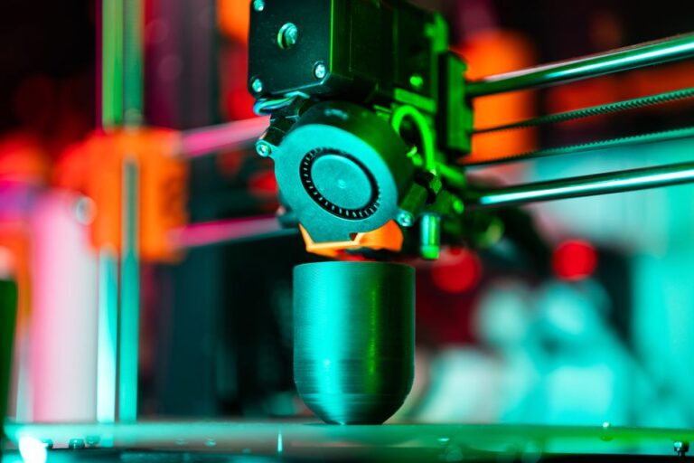 Le prototype OpenAI sort du brouillard, Jony Ive vise 2027 Close-up of a 3D printer creating a product in neon lighting.