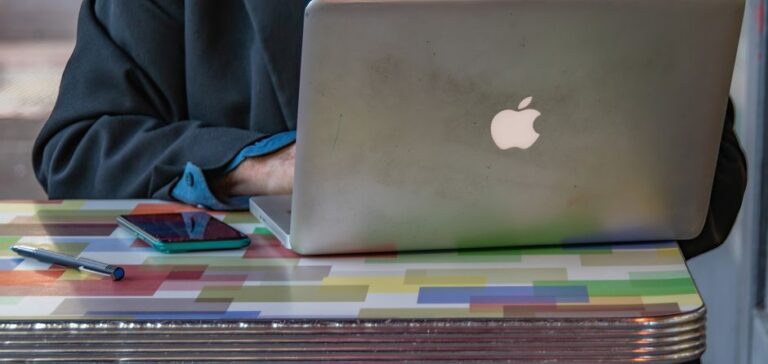 Apple Intelligence : le M1 rayé puis remis en ligne en 24 heures Close-up of a person using a laptop and smartphone on a colorful patterned table indoors.