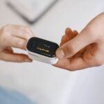 Close-up of a pulse oximeter on a finger, checking oxygen levels during a healthcare examination.