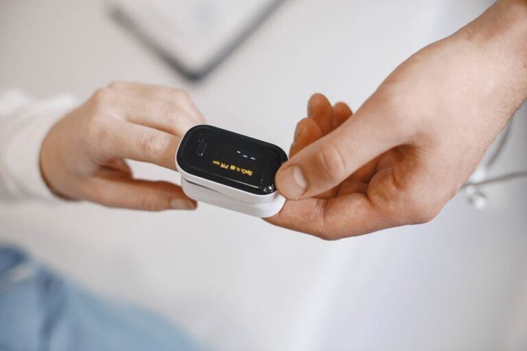 Close-up of a pulse oximeter on a finger, checking oxygen levels during a healthcare examination.