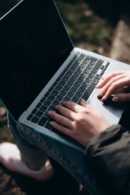 Close-up of a woman typing on a laptop outdoors, showcasing modern technology and mobility.