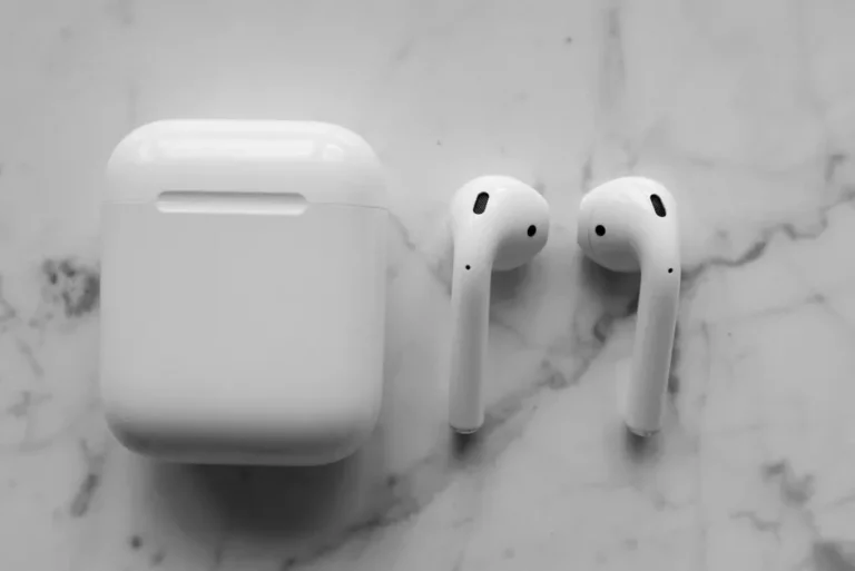 Close-up of wireless earbuds and charging case on a white marble background with soft lighting.